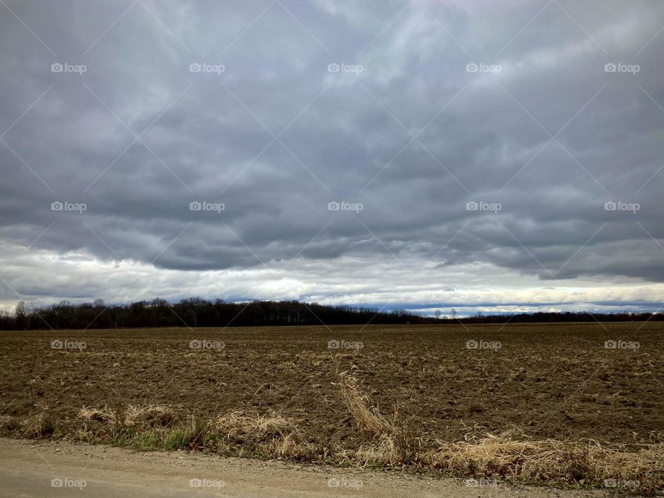 Gray clouds hang over a  Midwest Michigan field on a dirt road in a rual area on a fall day