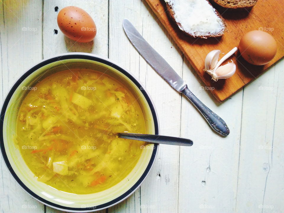 vegetable soup, bread and butter, eggs, a cup of tea and garlic on the table