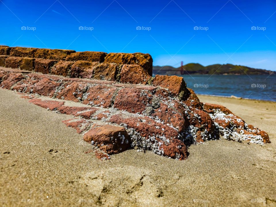 Brick wall emerged from the sand at Crissy Field in San Francisco California with a slight view of the Golden Gate Bridge in the background