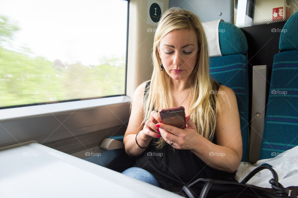Woman surfing on her phone when she traveling by train from Gatwick Airport to London.