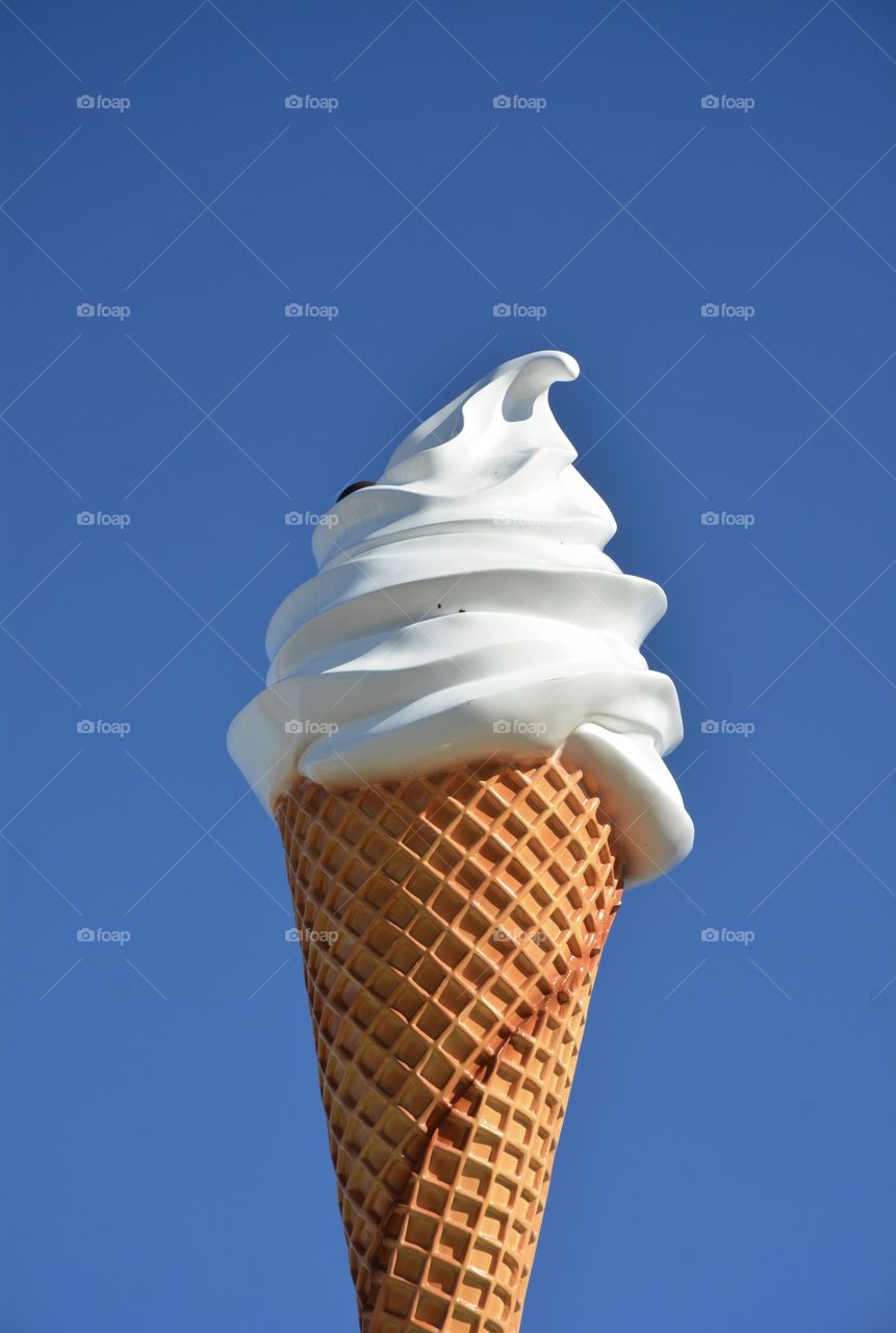 A large ice cream cone against a bright blue sky. 