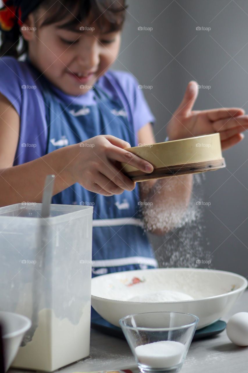 Cute little girl is sifting flour