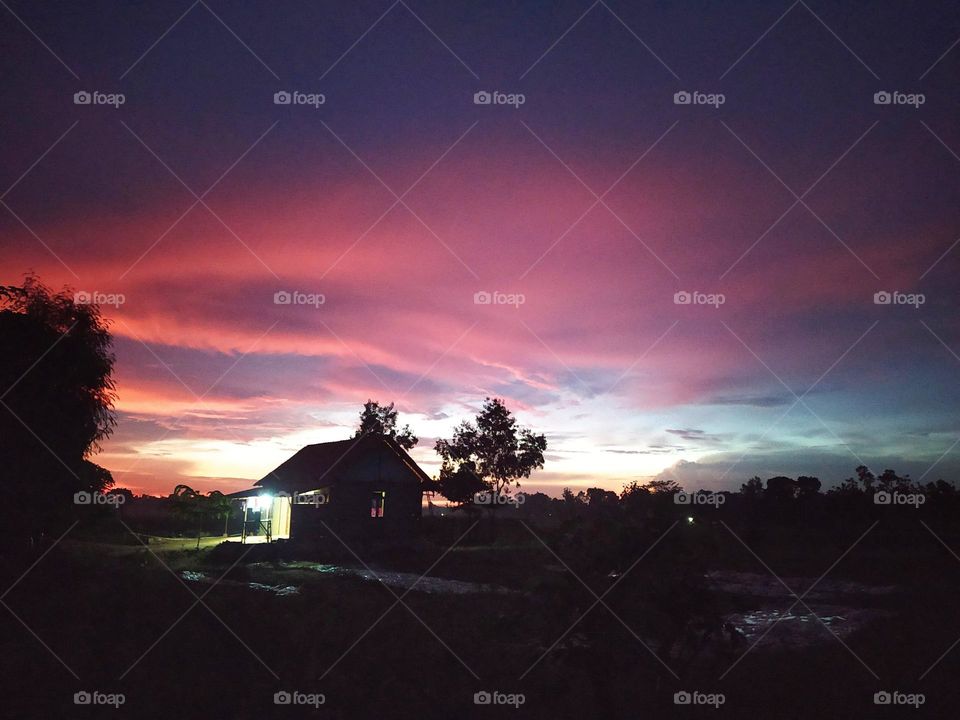 Beautiful view of dawn in a village near the rice fields, reddish light in the east sky.  Silhouette of a house and trees.