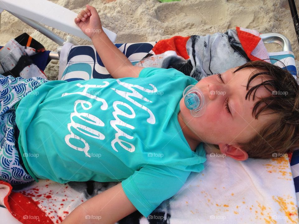 Boy sleeping on beach with pacifier