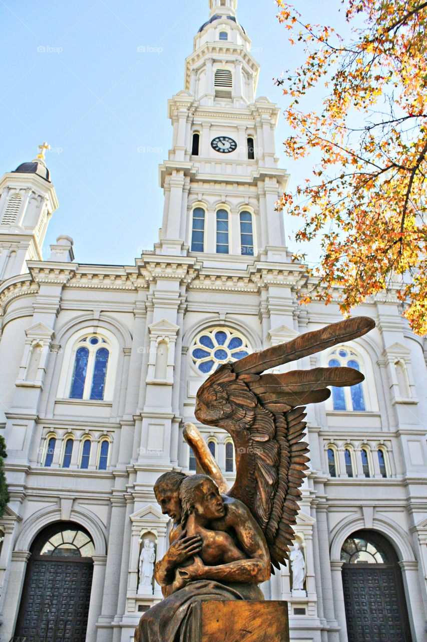 a protective angel statue in front of a building of worship, Outdoors, tree, fall, architecture