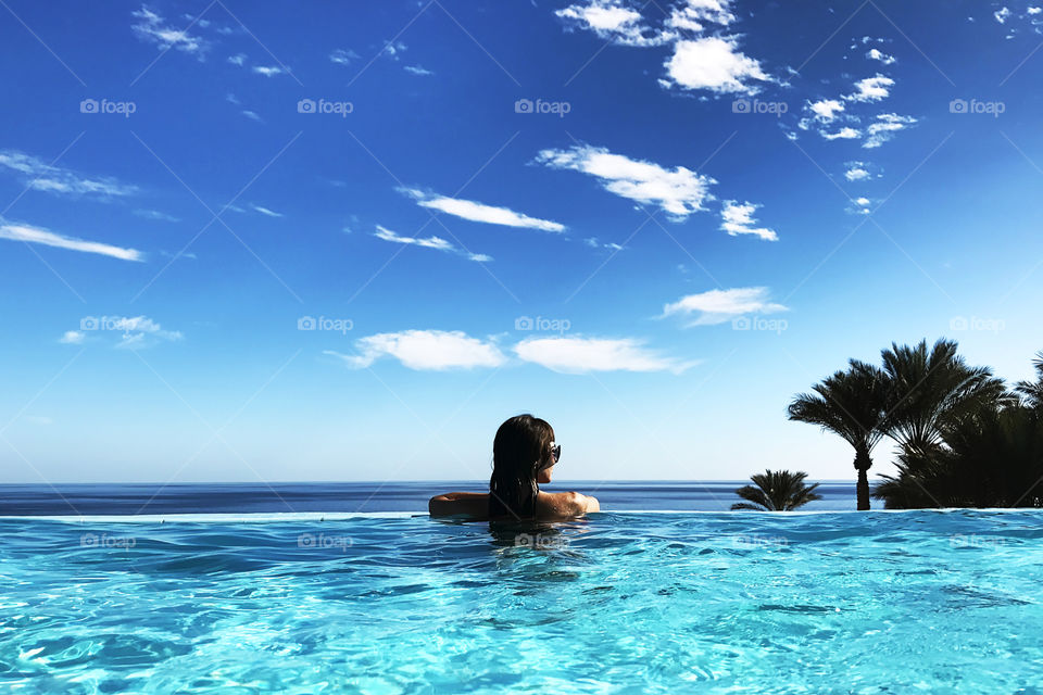 Young woman enjoying her summer tropical vacation at the swimming pool above the sea 