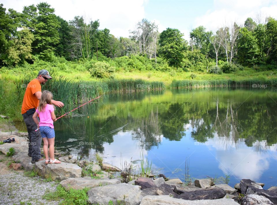 Father and daughter fishing in a pond on a summertime day 