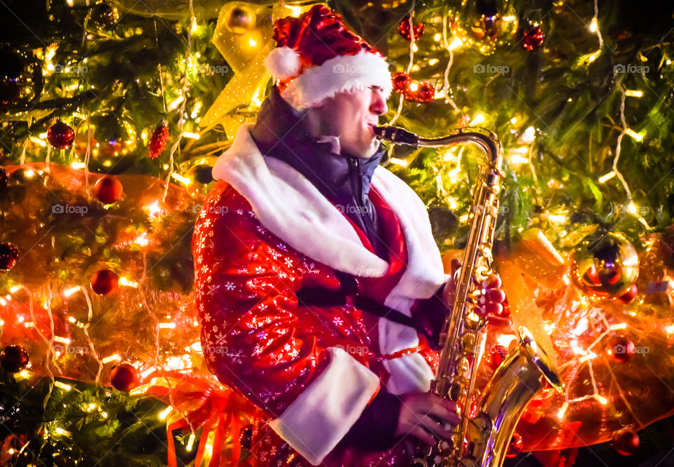 Cheerful Santa Claus Playing Saxophone Music In Front Of A Christmas Tree To Celebrate New Years Eve