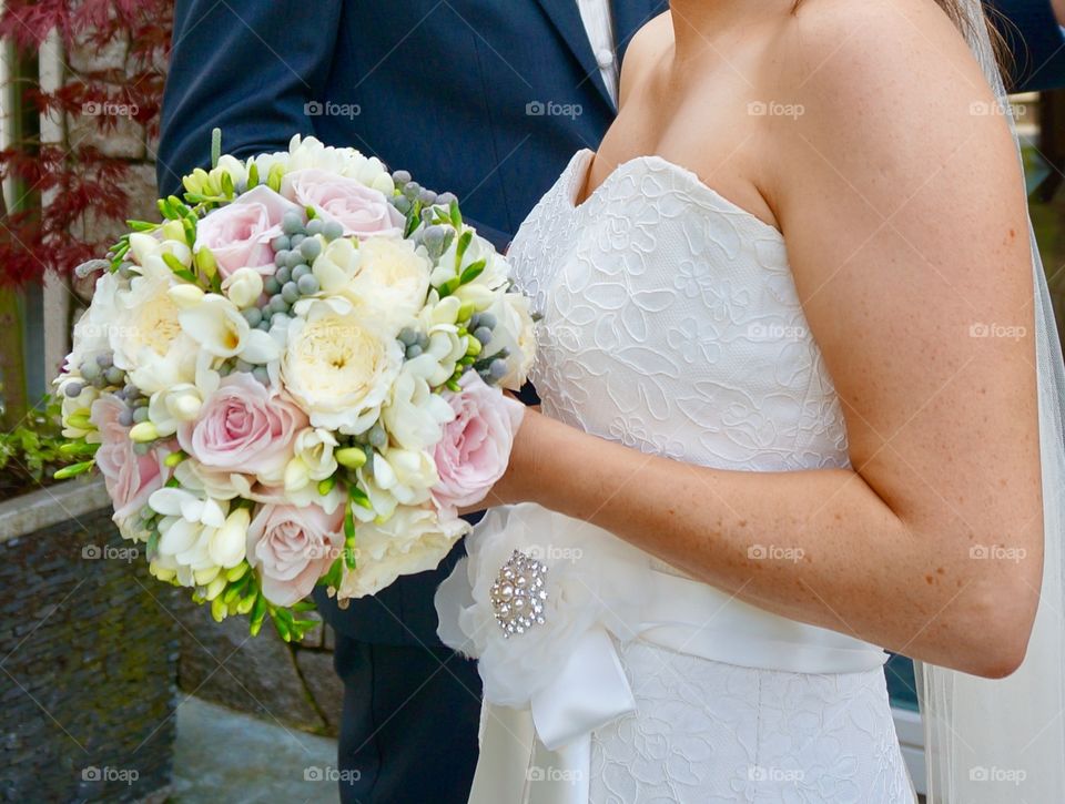 Mid section of bride and groom with flower bouquet