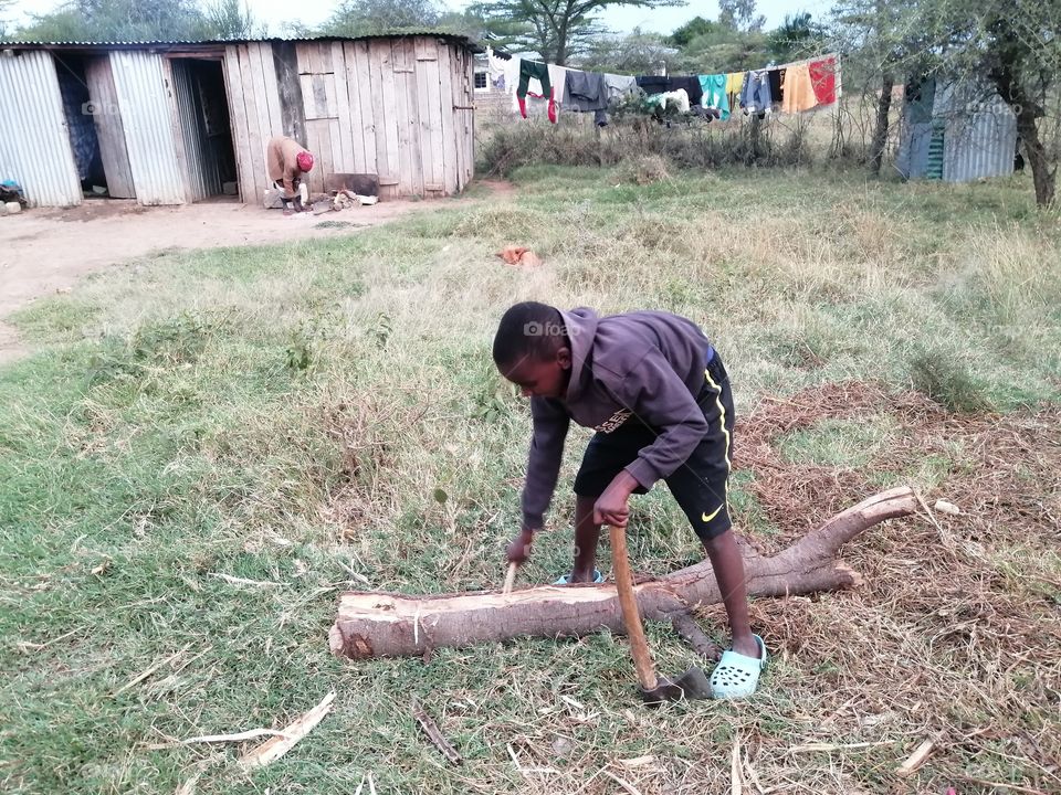 A young boy is learning how to split wood for his family fireplace