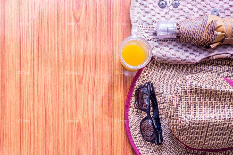 Ready to travel. Top view beach background of essential modern summer women accessories in wooden table. Sunglasses, umbrella, Straw hat, Beach bag and a glass of lime juice. Room for text on left.