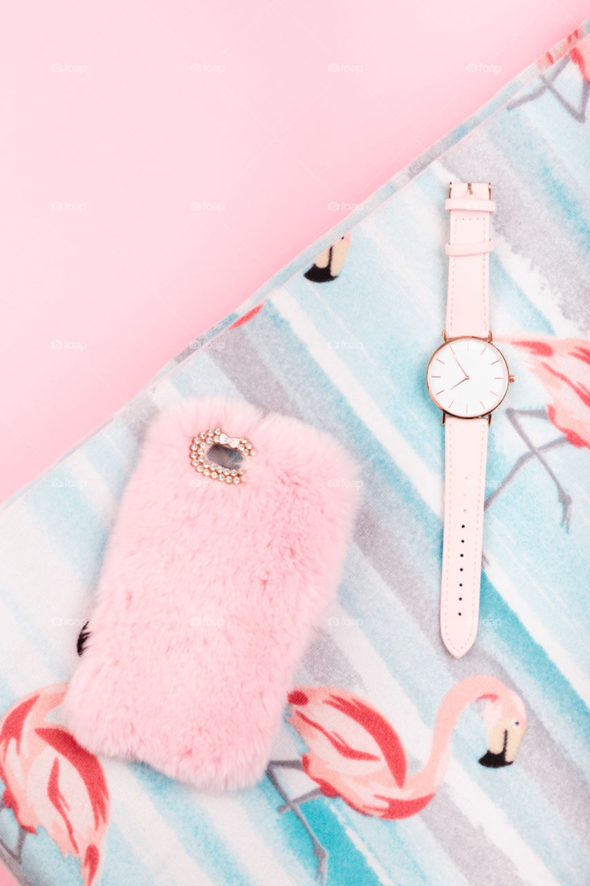 Mobile phone in pink case, watch with pink stripe on pink background
