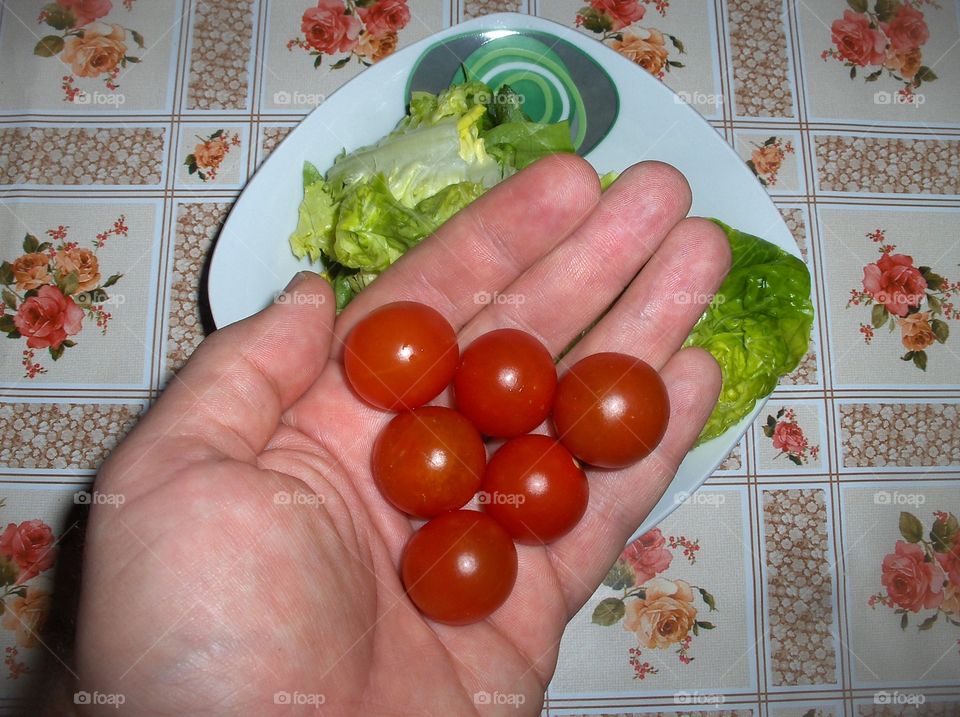 Hand holding 6 cherry tomatoes over salad.