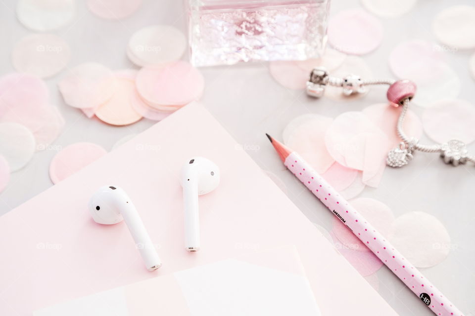 Flatlay items: perfume bottle, wireless headphones, notebook, pencil, star pink color, confetti lying on gray concrete background 