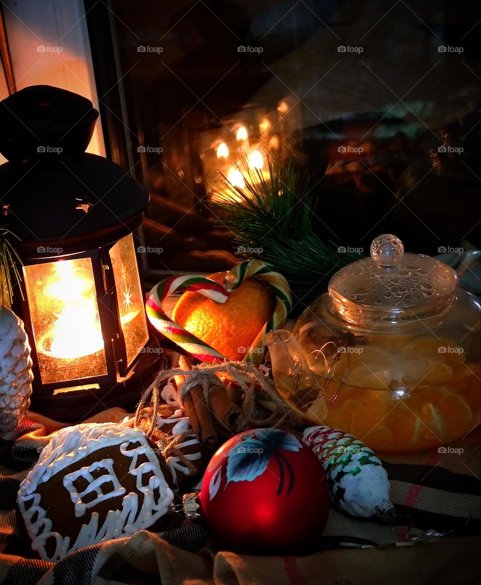 Waiting for Christmas.  Evening.  A burning candle in a lantern, gingerbread, tangerine, heart-shaped caramel canes, Christmas decorations and a teapot with tangerine tea.  A candle is reflected in the window