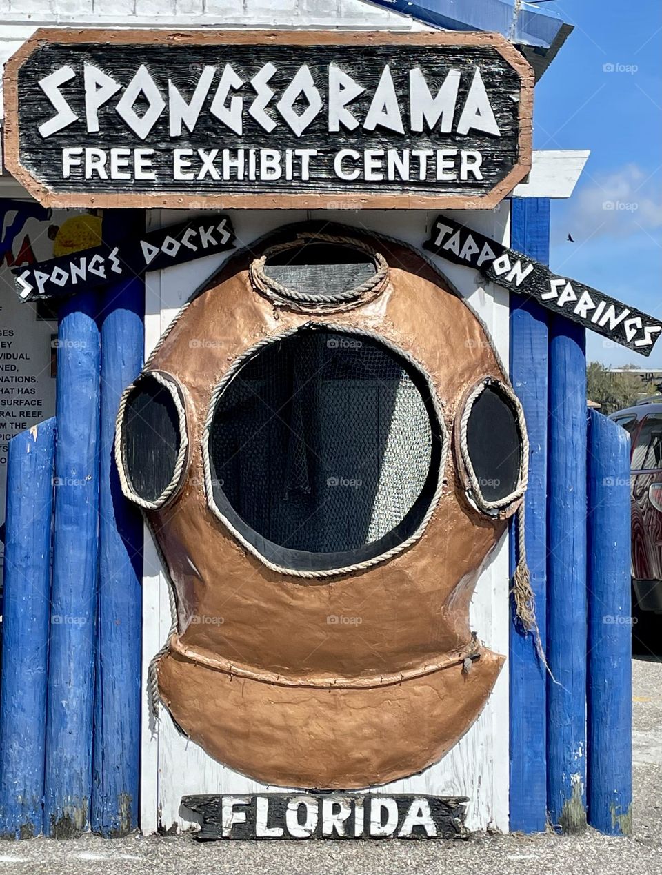 An eye-catching ad for the free Sponge Exhibit in Tarpon Springs, FL, features a vintage sponge diver's helmet as its focal point. The helmet stands out against the bold blue and white backdrop, symbolizing the deep Greek heritage of the town.