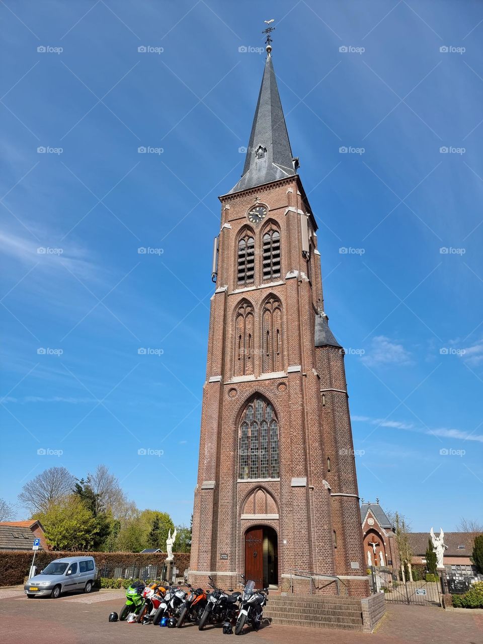 Catholic church in Gothic architectural style on a village square in the Netherlands. It is a sunny day and a row of motorbikes is parked in front of the church