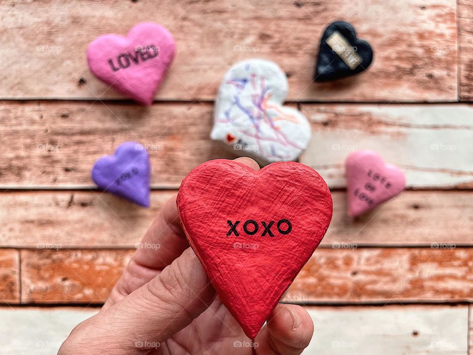 Making Valentines for family, woman holds Valentines Day handmade heart, making homemade gifts for grandparents, toddler and mother make salt dough hearts, woman’s hand holding handmade heart magnet, cute Valentines Day sayings on hearts