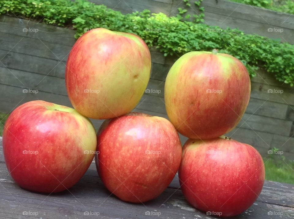 Apples stacked outdoors on wooden bench.