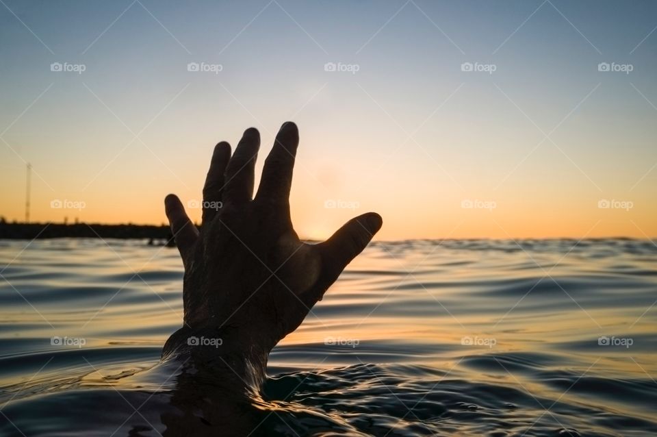 Hand rising out of the water at sunset