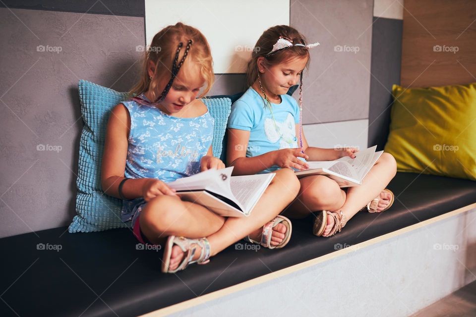 Two schoolgirls reading books in school library. Primary school students learning from books. Pupils doing homework. Children having fun with books in school club. Child curiosity