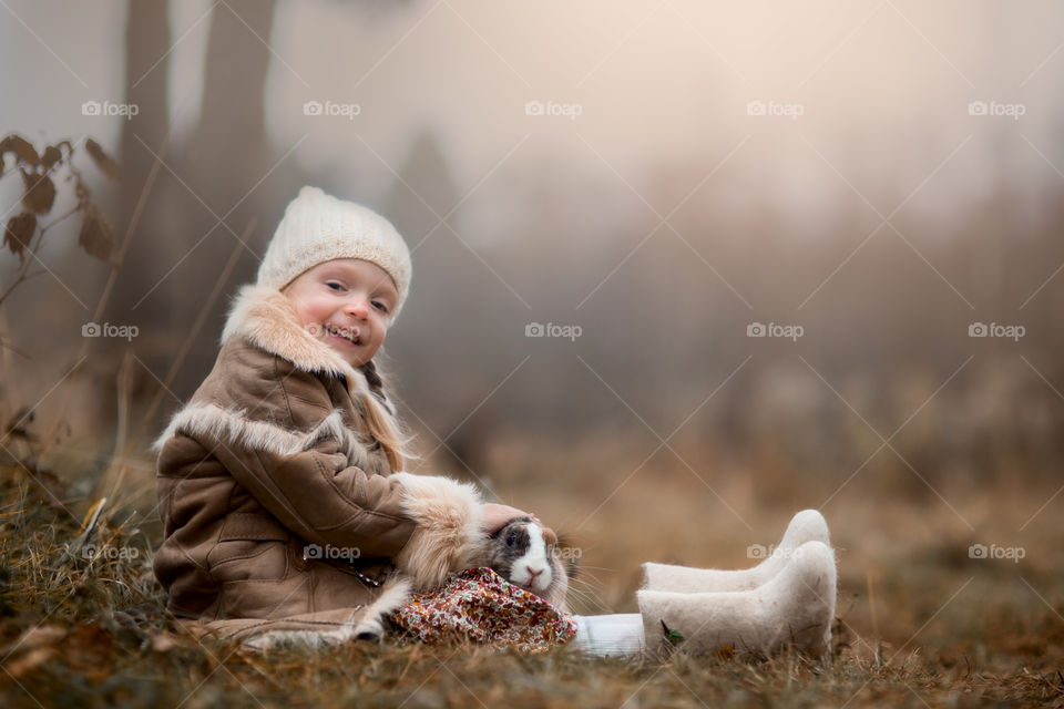 Cute Little girl with bunny in a forest at misty autumn evening 