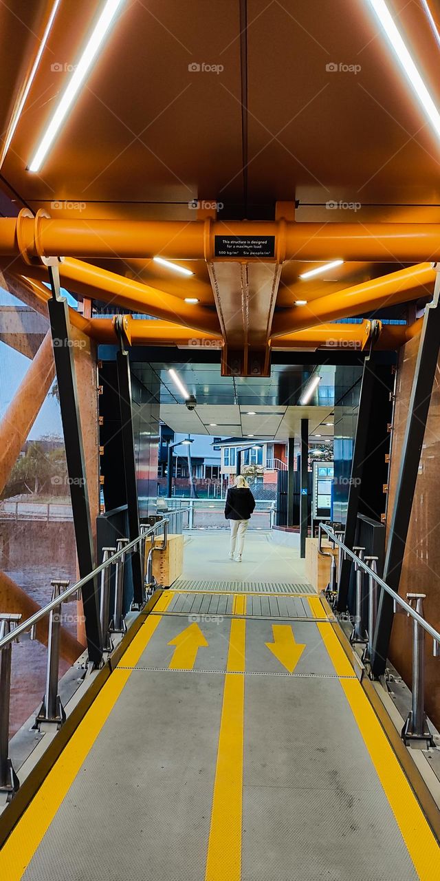 Blonde woman walking away on orange ferry terminal ramp.