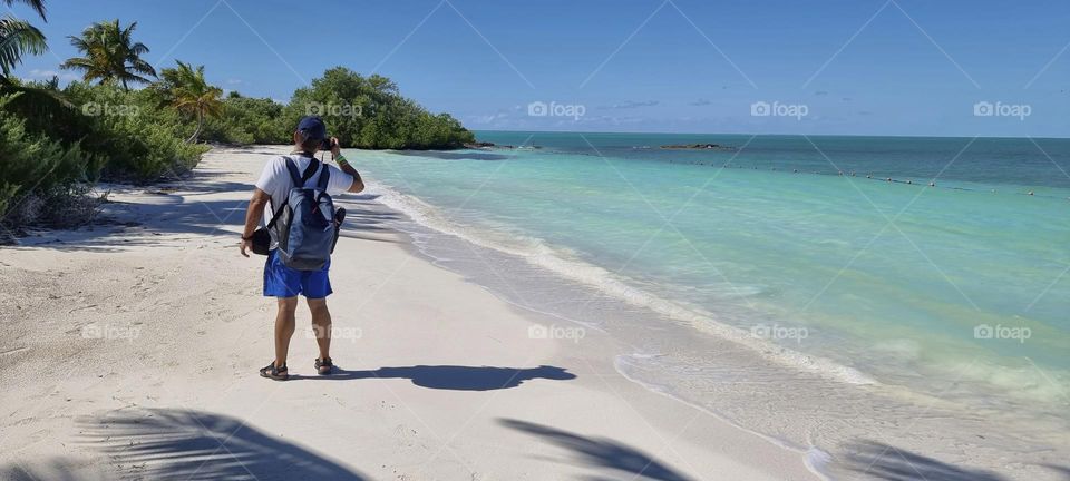 man taking photos on a paradisiacal beach with white sand and crystal clear waters