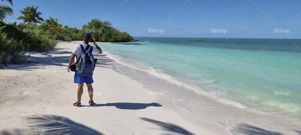 man taking photos on a paradisiacal beach with white sand and crystal clear waters