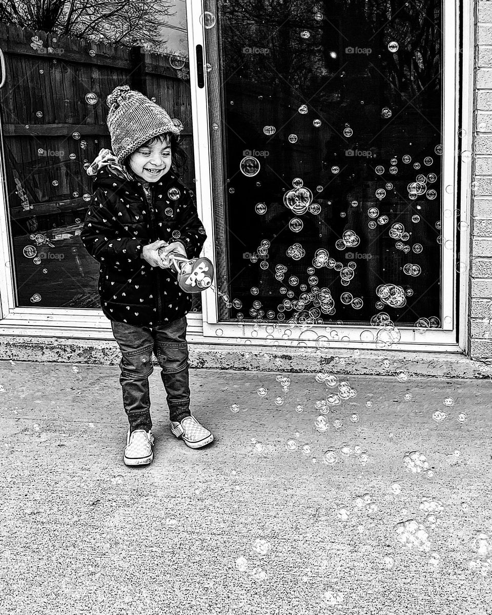 Black and white portrait of a toddler playing with bubbles in the winter, toddler girl blows bubbles in the winter time, monochrome bubbles in the air with toddler girl, fun activities with toddlers, portraits with smartphones 