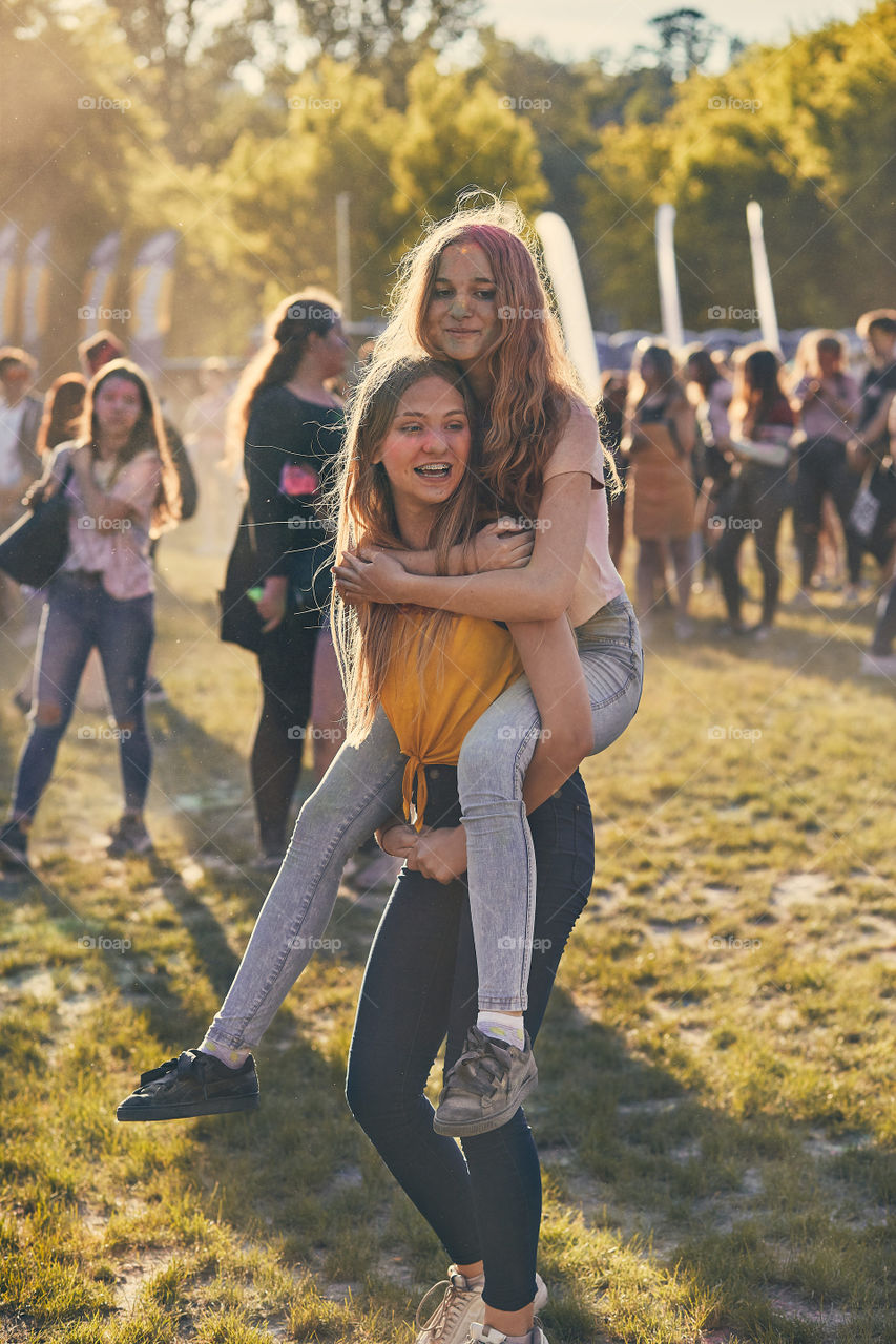 Portrait of happy smiling young girls with colorful paints on faces and clothes. Two friends spending time on holi color festival. Real people, authentic situations