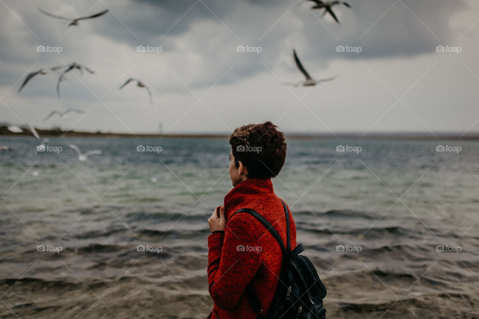 Girl in red coat looks at the seagulls and ocean 