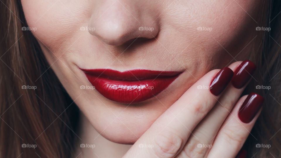 Woman's lips with magenta nail varnish on fingernails