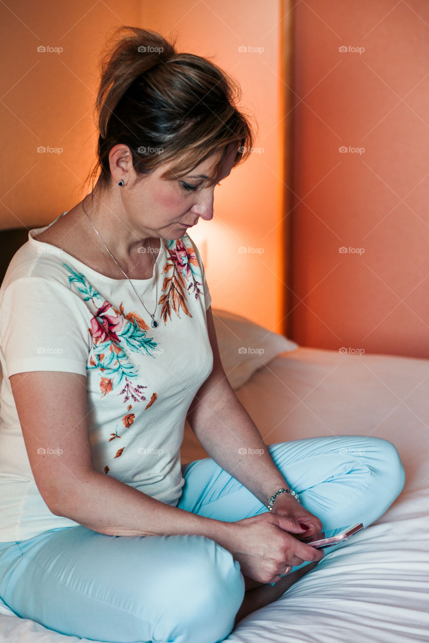 Young woman using smartphone while sitting in bed in bedroom