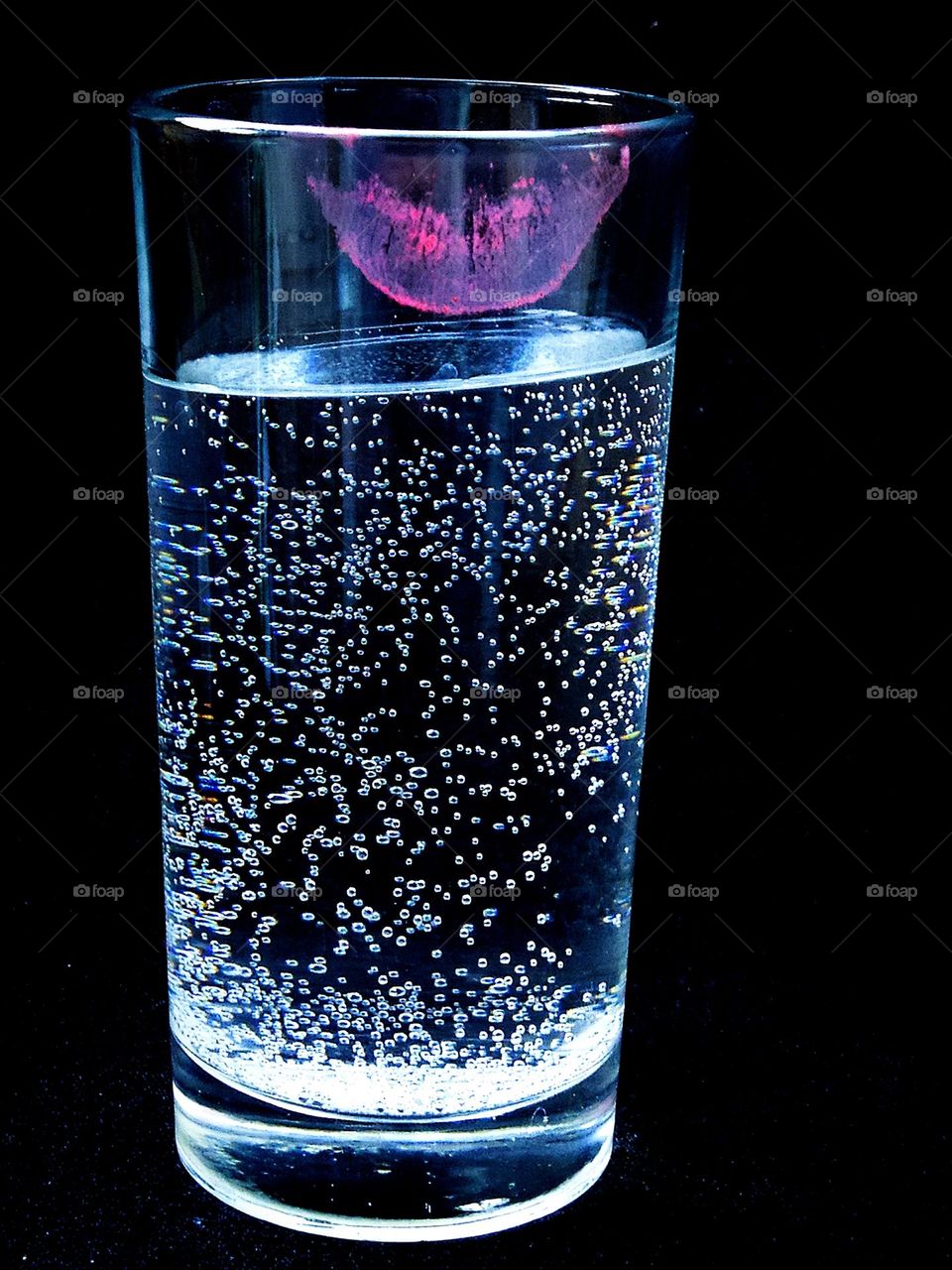 A glass of sparkling water.  There is a trace of purple lipstick lips on the glass.  Black background