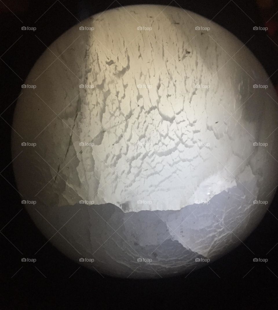 A Selenite crystal ball in the darkness with light shining through.