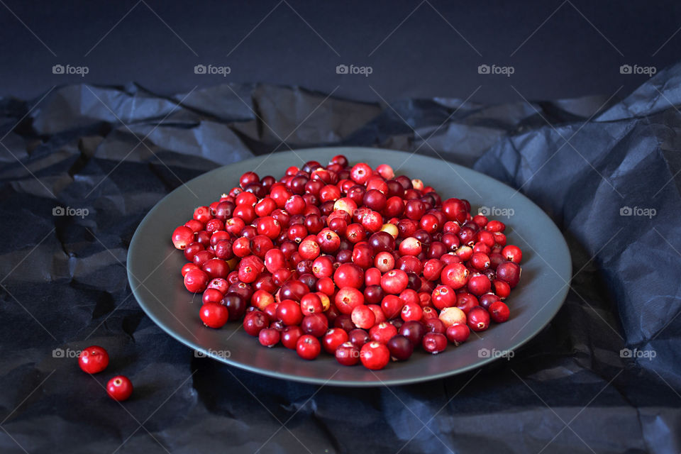 Berries of ripe red cranberries on a black plate on black crumpled paper. Food for health and raising immunity in the cold season. The harvest of autumn berries. Horizontal orientation