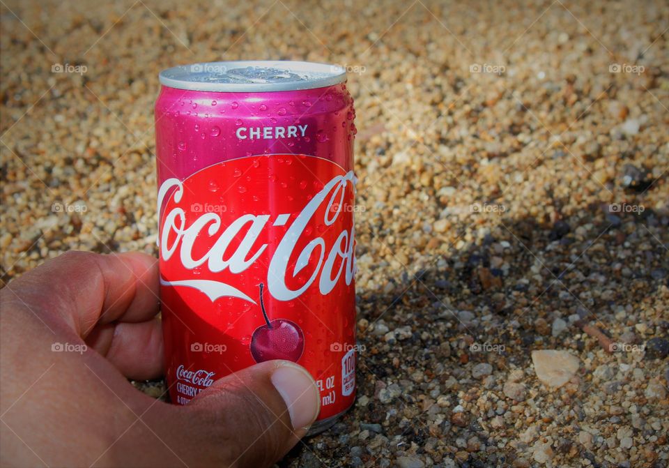 hand holding a can of Cherry Coke soda on the sands the beach