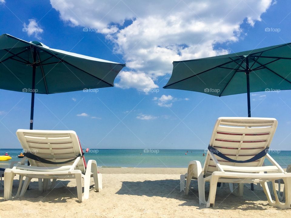 Two empty sunbeds with umbrellas on a sunny day at the beach