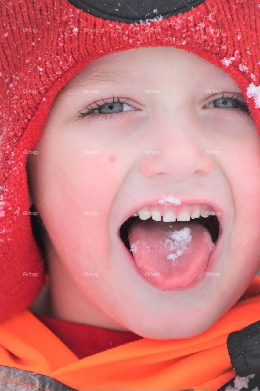 A close-up of a cute little boy with bright blue eyes catching falling snow on his tongue. 