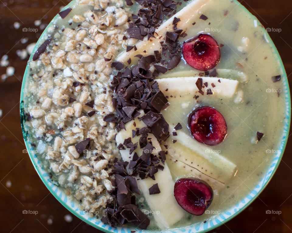 Antioxidant rich gourmet dark chocolate sprinkled on banana cherry oatmeal fresh fruit superfoods smoothie bowl with bee pollen and chia seed 