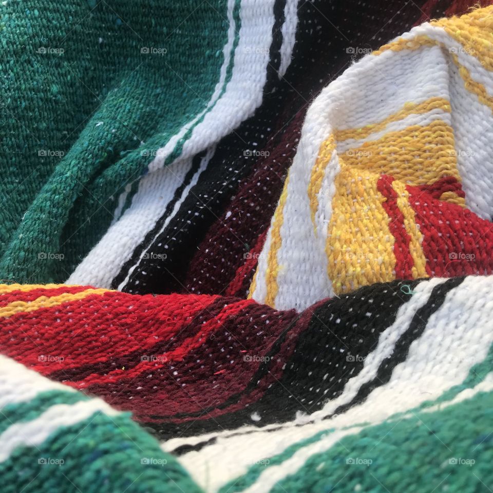 The colorful and flowing fabric of a falsa blanket, unfolded and warming toes by the beach. 
