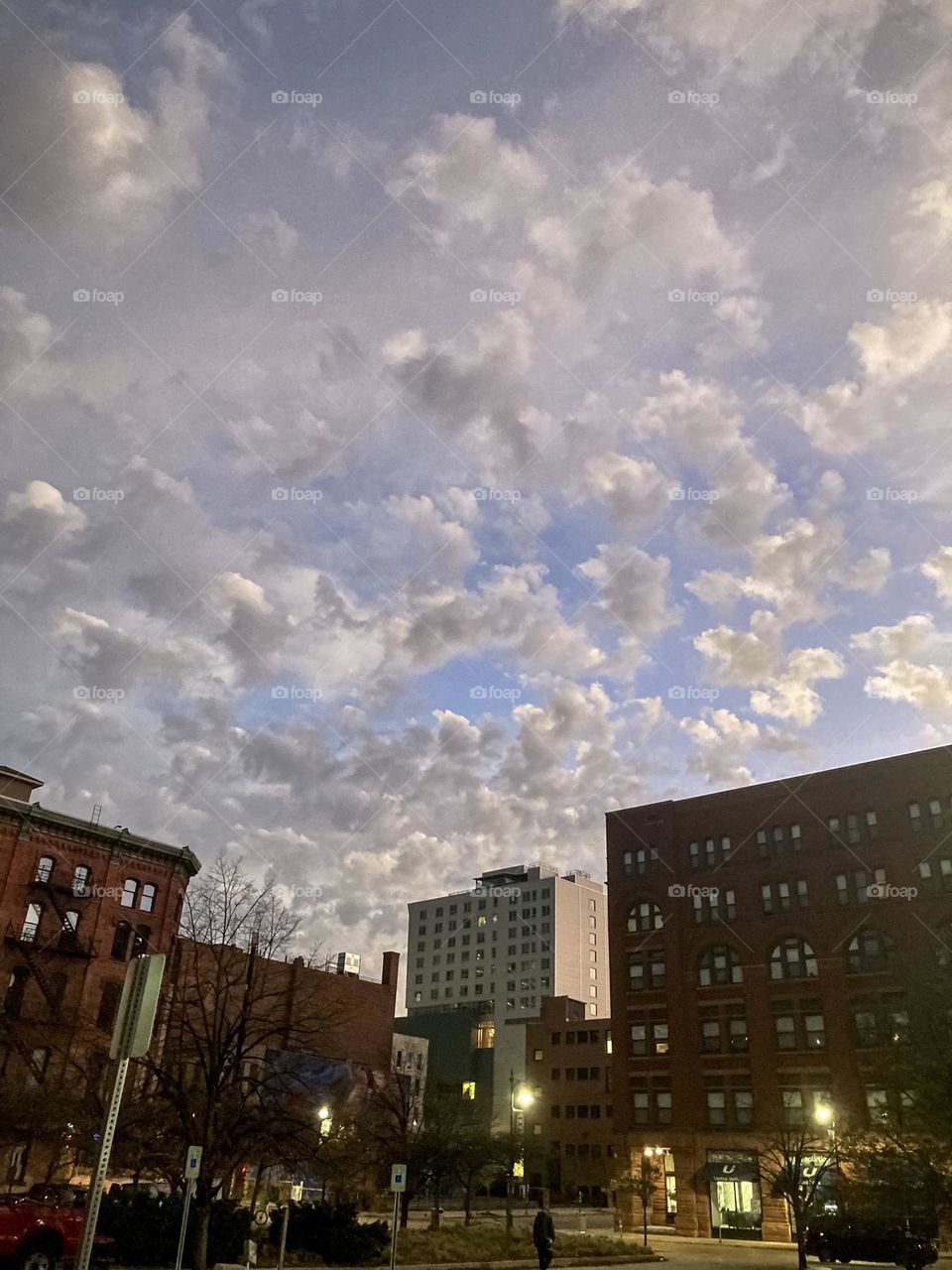 Sun rise lights up the the blue sky and white clouds in downtown Grand Rapids Michigan where the street lights are still illuminated from the night. 