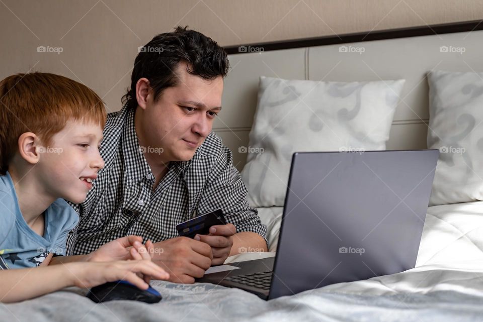 Red-haired boy with his father watching a movie on a laptop lies on the bed