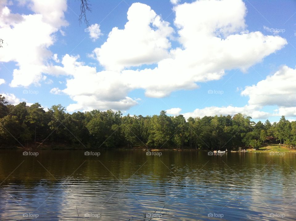 Summer at the lake. Sunny sky, puffy white clouds in a blue sky over a lake