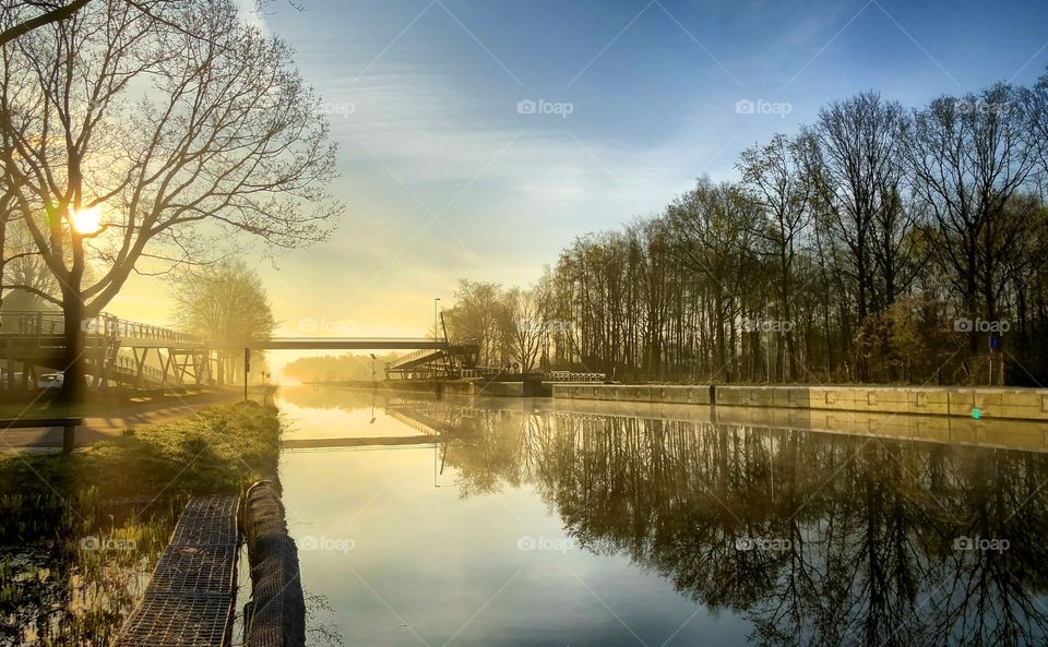 Golden sunrise or sunset reflected in the water of the river or canal that runs through the woods