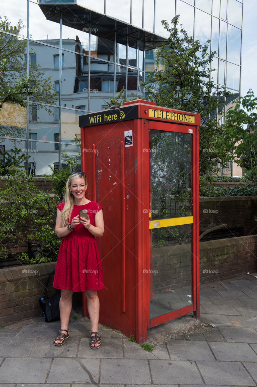Woman 30 years old looking at her phone and social media at at WiFi spot at a telephone booth in London near Euston Square.