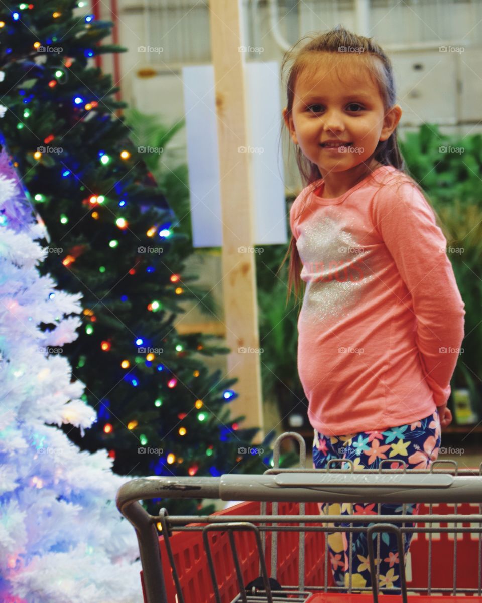 Little girl in shopping cart near christmas tree