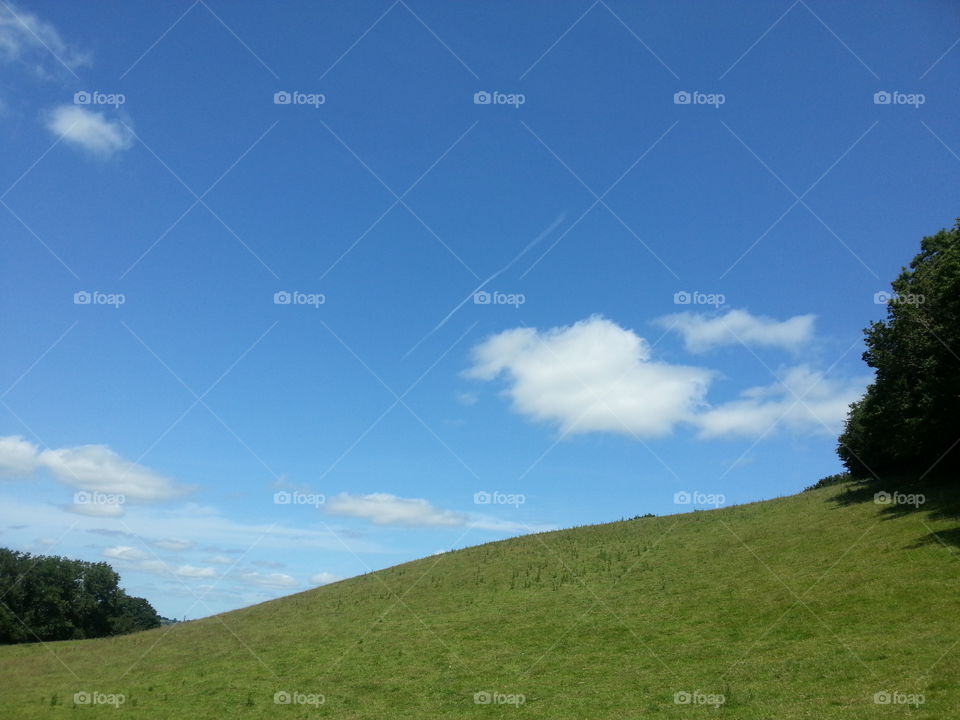 Big blue sky, hillside, some clouds and a contrail