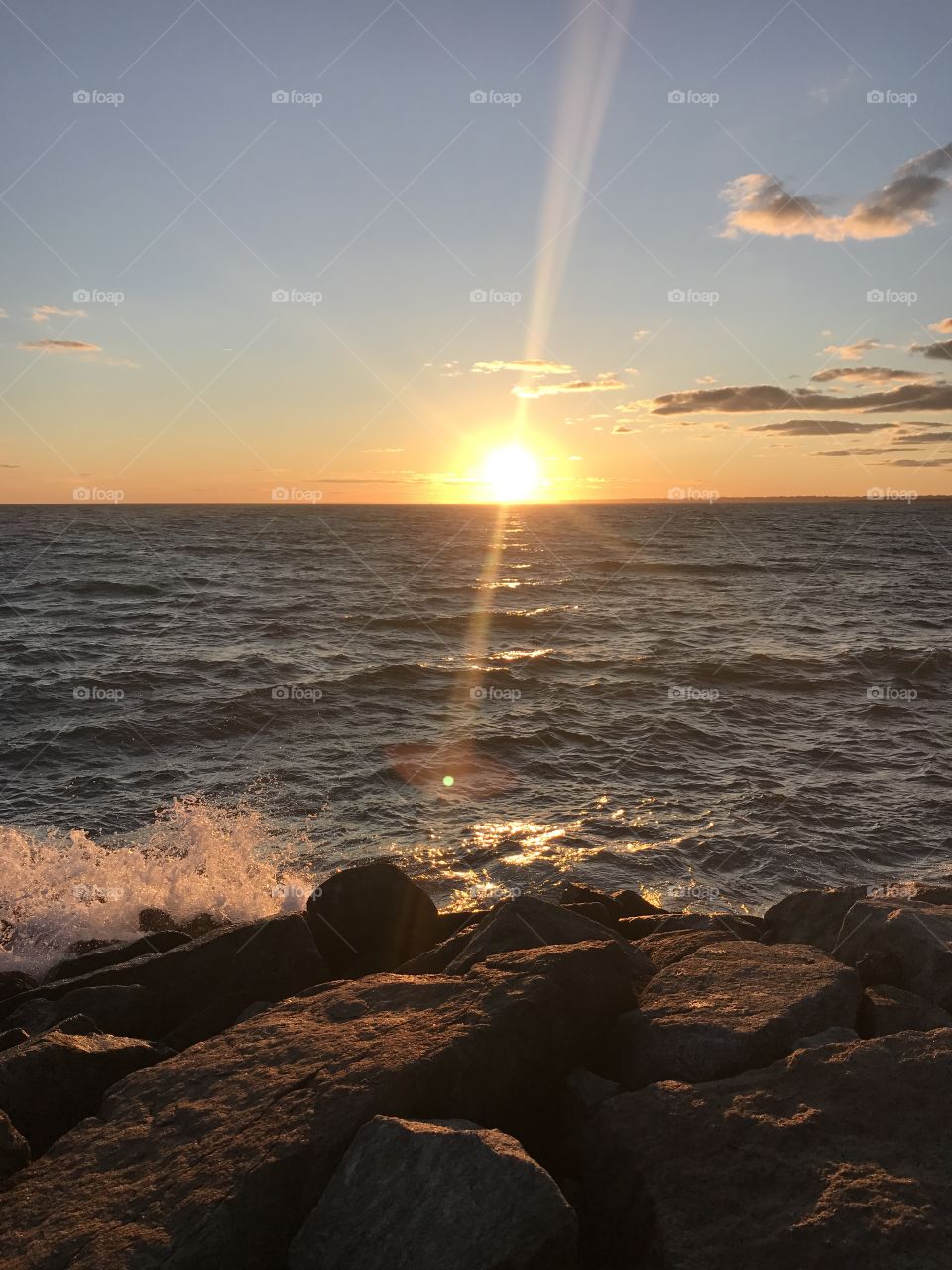 Sunsets in Rhode Island. Waves crashing upon the rocks with the sun shining above as it sets 